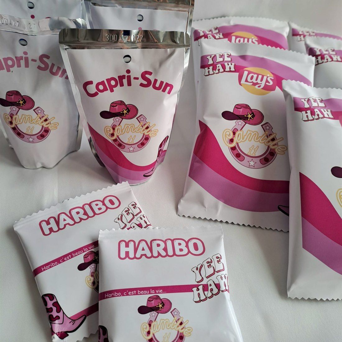 Gourdes, sachets de chips et de bonbons habillés d'étiquettes roses sur un thème cowboy : chapeau, fer à cheval et botte.