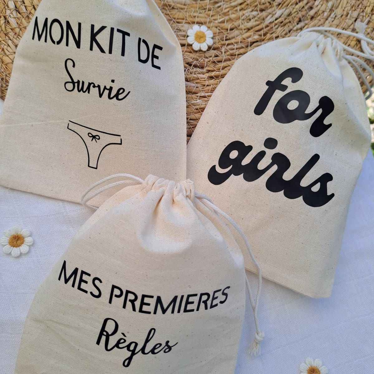 Trois pochons en coton écru à cordon coulissant, floqués en noir : « Mon kit de survie » et « Mes premières règles », illustrés d'une culotte, et « for girls » en lettres arrondies.