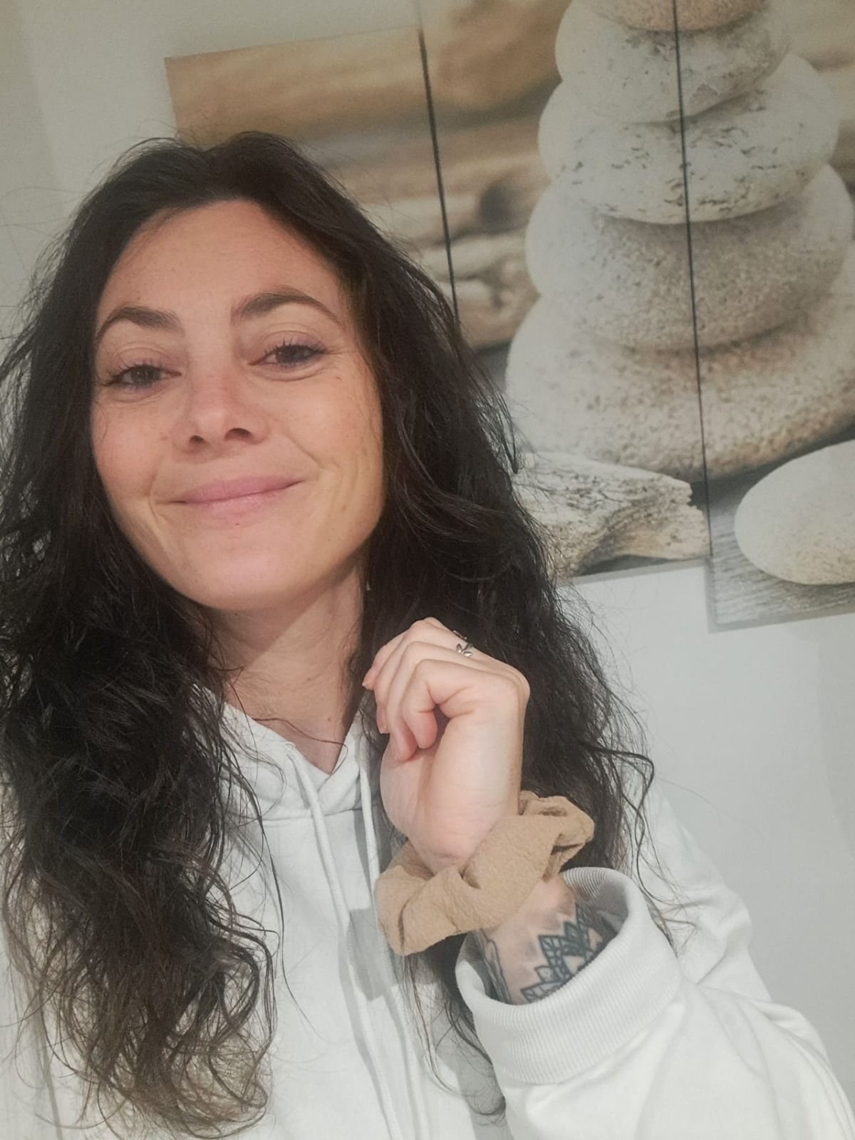 Floriane, souriante, longs cheveux bruns bouclés et sweat blanc, devant un tableau de galets empilés.